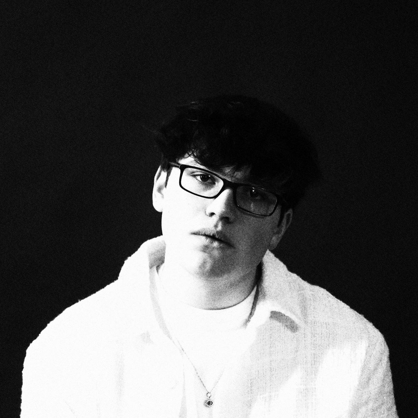 Promotional photo for "house of glass" featuring Colleen Angel, which sees a black and white head shot of Rob Eberle who is wearing a white jacket over a white t-shirt, with glasses.