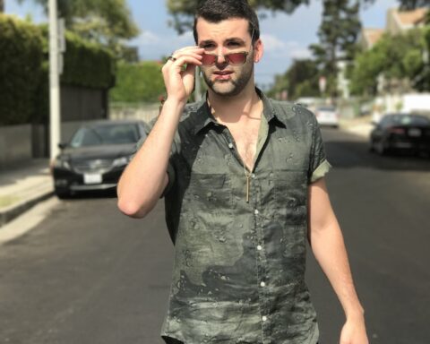 Promotional photo for "Over" which sees Ducktail in the middle of a street, wearing a camo green shirt and sunglasses which he has pulled down his nose to look at the camera.