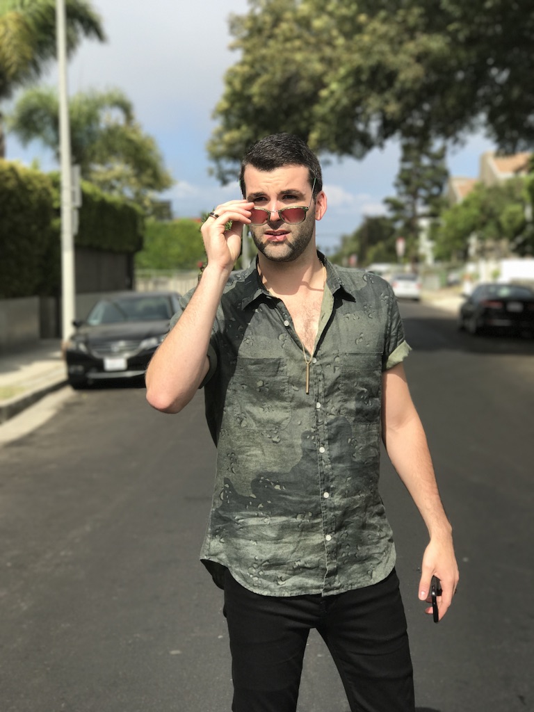 Promotional photo for "Over" which sees Ducktail in the middle of a street, wearing a camo green shirt and sunglasses which he has pulled down his nose to look at the camera.