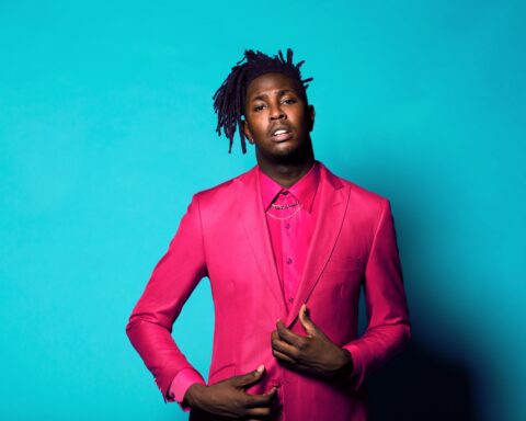 Promotional photo for "Summer Pack" EP which sees Mike Taylor dressed in a bright pink two-piece suit, standing against a bright blue background.