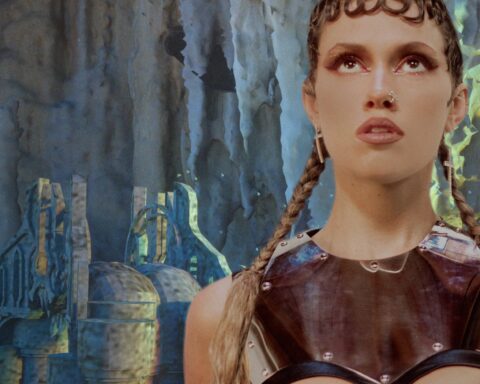 Promotional photo for "Low Jewel" which sees ROWA standing to the right with a grey wall face behind her, dressed up in gladiator-like armour.