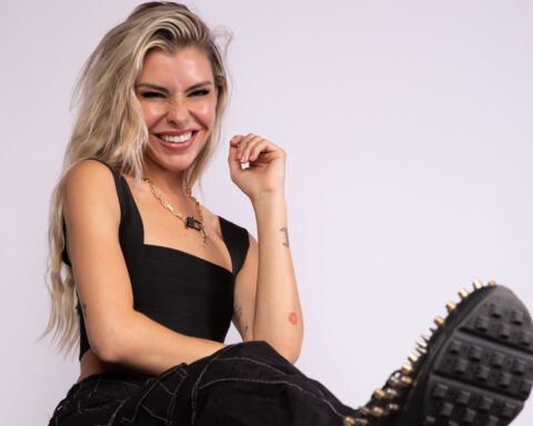 Promotional photo for "Munca" that sees Sam Blacky posing at a photo studio, sitting down against a white background. She's wearing a black halter top with black cargo trousers and black boots, and she's laughing as she leans backwards.