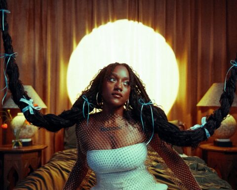 Promotional photo for "Mirror" which sees Aryeè The Gem sitting on a bed wearing a white dress and a diamante netting top, with her long black hair in two bunches which are braided and are attached to the roof by their ends, to create two plait swings, reminding us of a black-haired Rapunzel.
