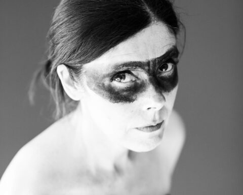 Black and white promotional photo for "Dark Horse" which is a headshot of Maria Wilman with her hair tied back and a black face-painted eye-mask marking on her face.