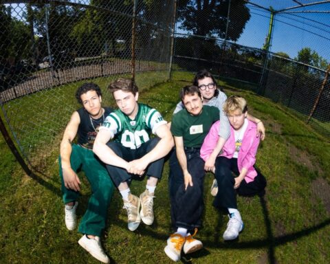 Promotional photo for "Sad Sugar" which sees the band New Friends sitting on a patch of grass wearing sporty clothes.